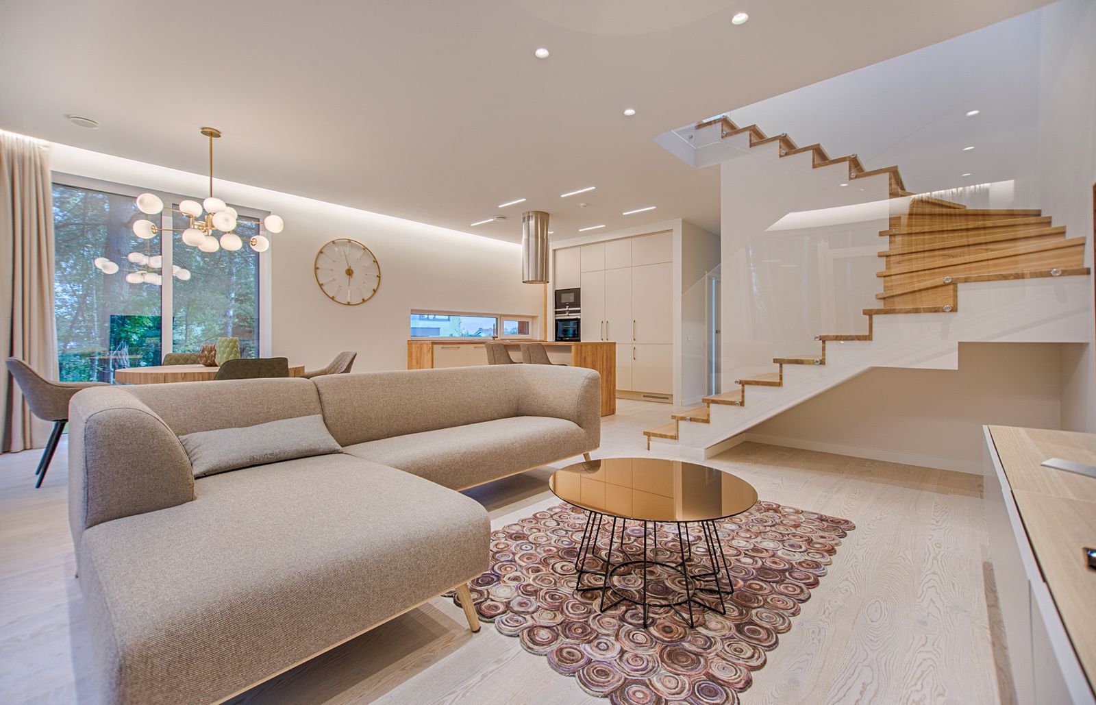 A bright, spotless open-plan living room with a soft sofa, warm wood staircase, and clean kitchen beyond — a home cared for by Victoria's Cleaning in St. George, Utah