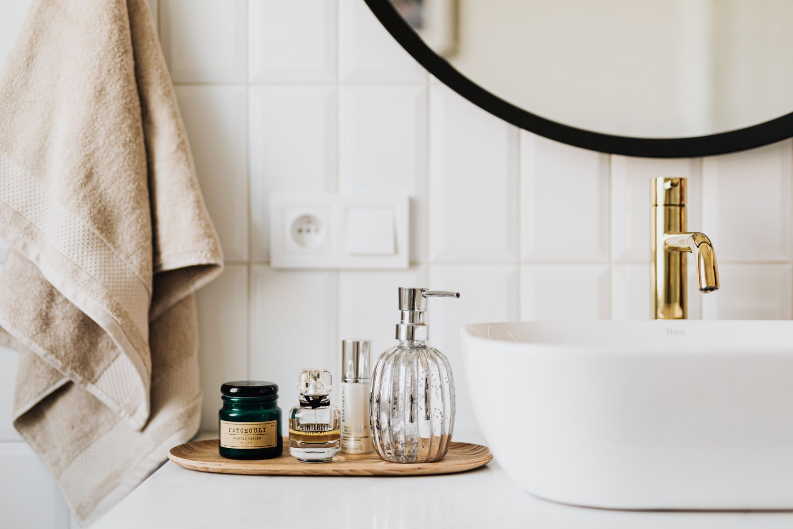 An elegant bathroom vanity with a folded towel, gold faucet, scented candle, and softly styled details
