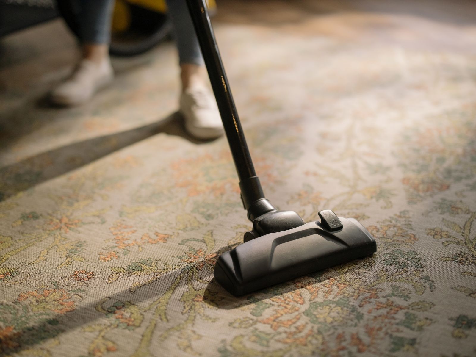 A cleaner running a vacuum across a patterned rug, leaving a clean track behind