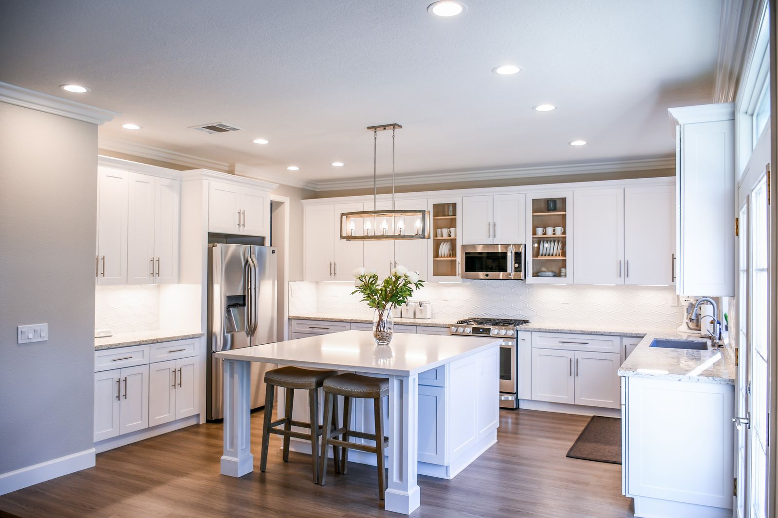 A pristine white kitchen with a clean island, polished countertops, and fresh flowers in a vase